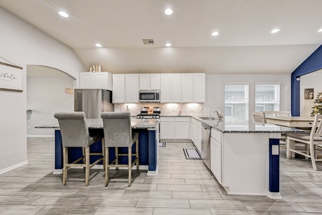 kitchen with lofted ceiling, a kitchen island, white cabinetry, appliances with stainless steel finishes, and light stone counters