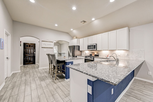 kitchen with a kitchen bar, kitchen peninsula, appliances with stainless steel finishes, white cabinets, and sink