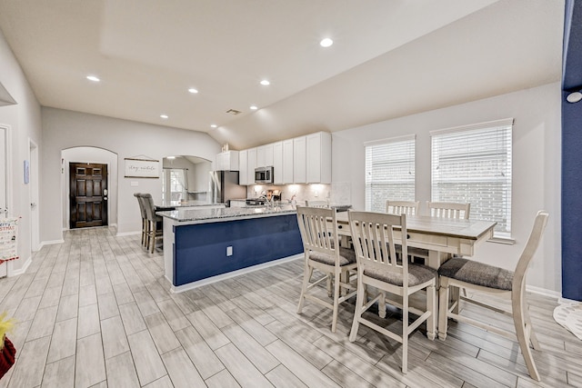 kitchen featuring lofted ceiling, decorative backsplash, white cabinetry, stainless steel appliances, and light stone counters