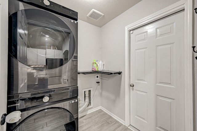 laundry area with a textured ceiling and stacked washer / dryer