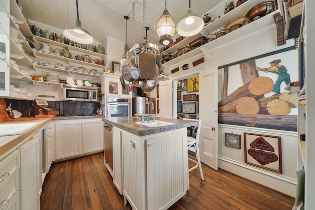 kitchen with a kitchen bar, appliances with stainless steel finishes, sink, decorative light fixtures, and an island with sink