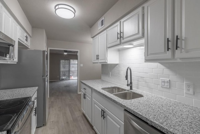 kitchen featuring sink, appliances with stainless steel finishes, light hardwood / wood-style floors, light stone counters, and white cabinetry