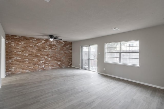 spare room with wood-type flooring, ceiling fan, and brick wall