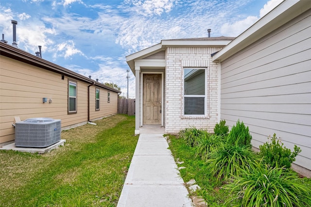 view of exterior entry with central AC and a lawn