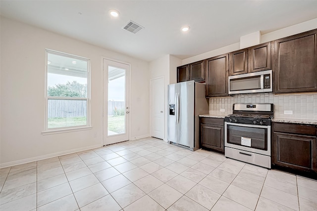 kitchen featuring light stone countertops, stainless steel appliances, tasteful backsplash, dark brown cabinets, and light tile patterned floors