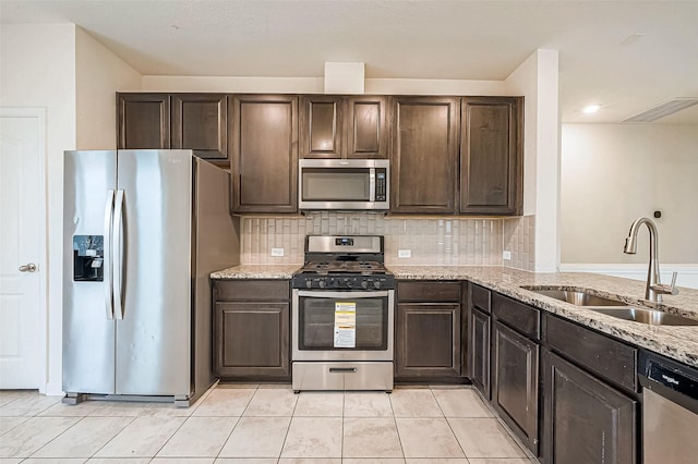 kitchen with decorative backsplash, light stone counters, dark brown cabinets, stainless steel appliances, and sink