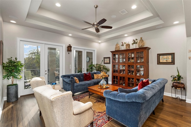 living room with a raised ceiling, dark hardwood / wood-style flooring, ceiling fan, and french doors