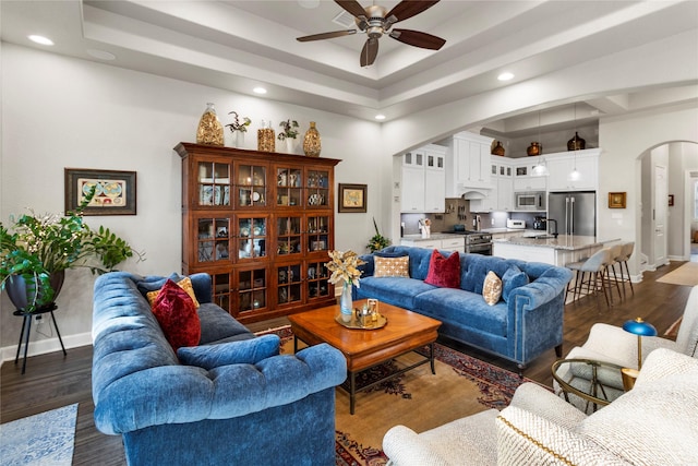 living room with a tray ceiling, ceiling fan, sink, and dark wood-type flooring