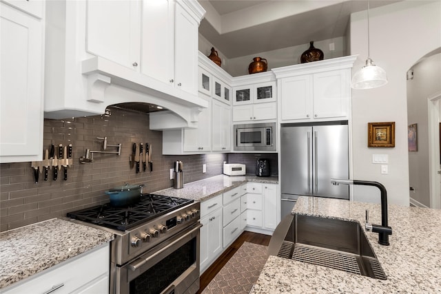 kitchen with light stone countertops, decorative backsplash, high end appliances, pendant lighting, and white cabinetry