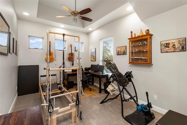 exercise room featuring a tray ceiling, ceiling fan, and dark colored carpet