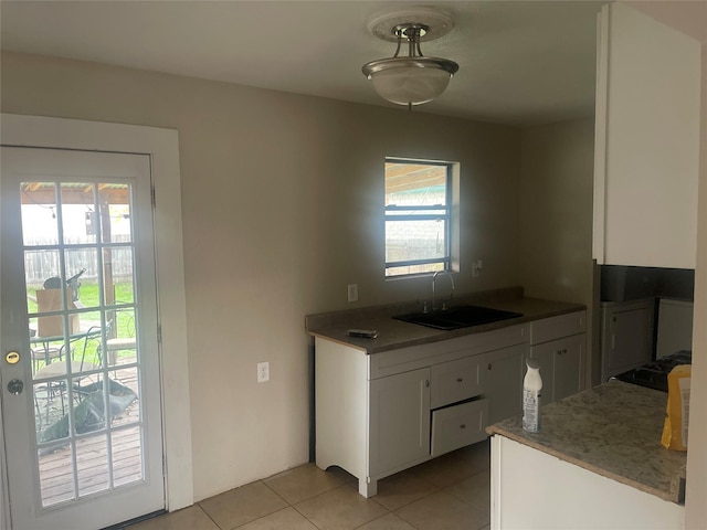 kitchen featuring sink, white cabinets, stovetop, and light tile patterned floors