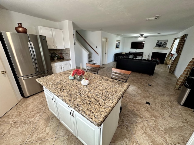 kitchen with white cabinets, a center island, light stone countertops, and stainless steel refrigerator