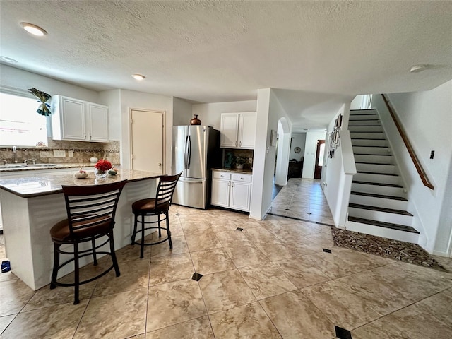 kitchen featuring a kitchen bar, stainless steel fridge, backsplash, white cabinets, and a kitchen island