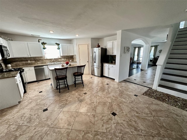 kitchen with a center island, a kitchen breakfast bar, tasteful backsplash, white cabinetry, and stainless steel appliances