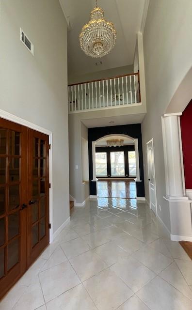 foyer with french doors, a towering ceiling, light tile patterned floors, and an inviting chandelier