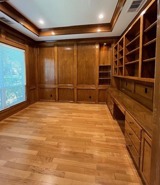 interior space featuring light wood-type flooring, a tray ceiling, crown molding, built in desk, and wood walls