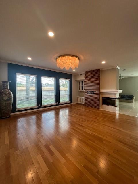 unfurnished living room featuring a healthy amount of sunlight, wood-type flooring, and ornamental molding