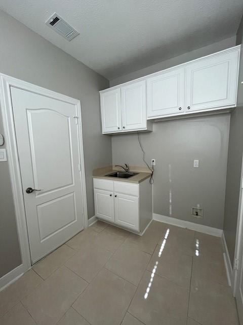 laundry room featuring sink, light tile patterned floors, and cabinets