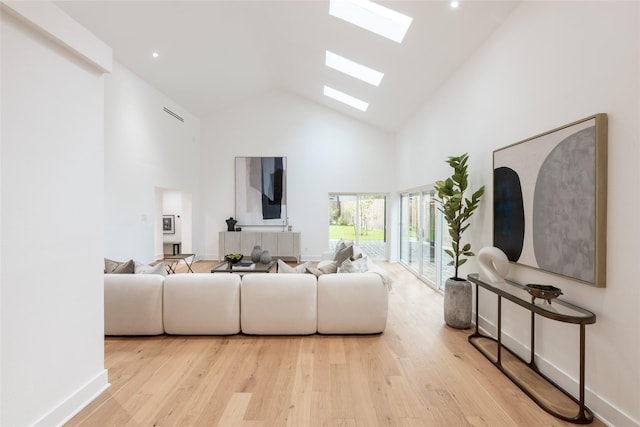 living room with a high ceiling, a skylight, and light hardwood / wood-style flooring