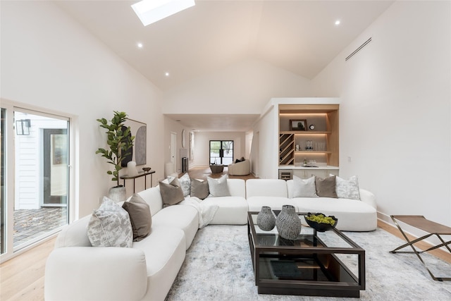 living room with a skylight, high vaulted ceiling, and light wood-type flooring