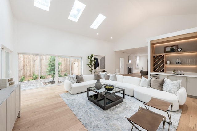 living room featuring a skylight, high vaulted ceiling, and light hardwood / wood-style floors