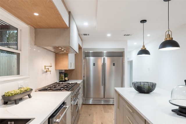 kitchen with premium appliances, light hardwood / wood-style floors, light stone counters, and decorative light fixtures