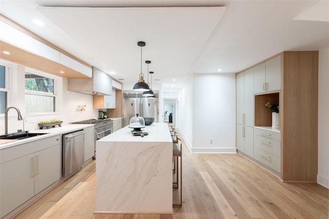 kitchen with appliances with stainless steel finishes, sink, light hardwood / wood-style flooring, a kitchen island, and hanging light fixtures