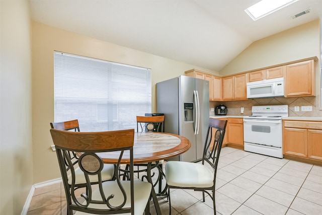 kitchen with light brown cabinetry, tasteful backsplash, vaulted ceiling with skylight, white appliances, and light tile patterned floors