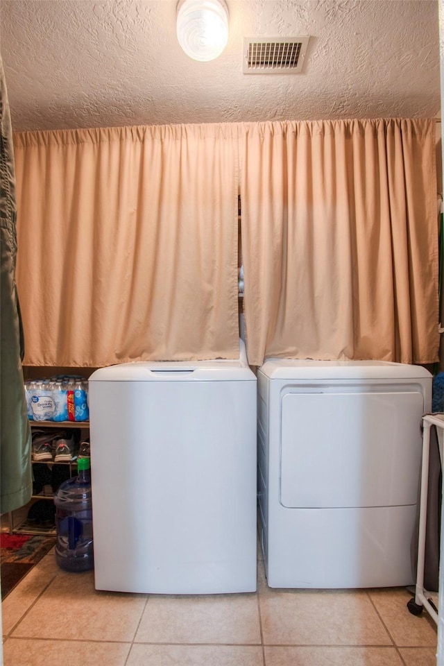 washroom featuring washing machine and dryer, light tile patterned floors, and a textured ceiling