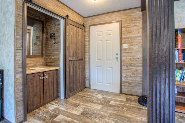 interior space featuring wood walls, a barn door, light hardwood / wood-style floors, and a textured ceiling