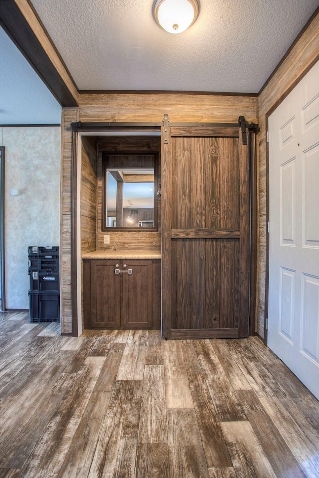 interior space with a barn door, a textured ceiling, wooden walls, dark brown cabinets, and hardwood / wood-style flooring