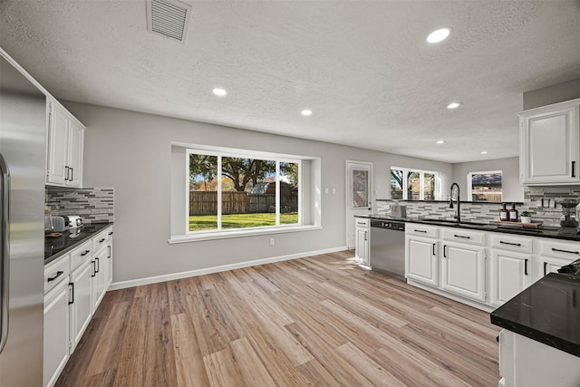 kitchen featuring appliances with stainless steel finishes, light wood-type flooring, backsplash, a textured ceiling, and white cabinetry