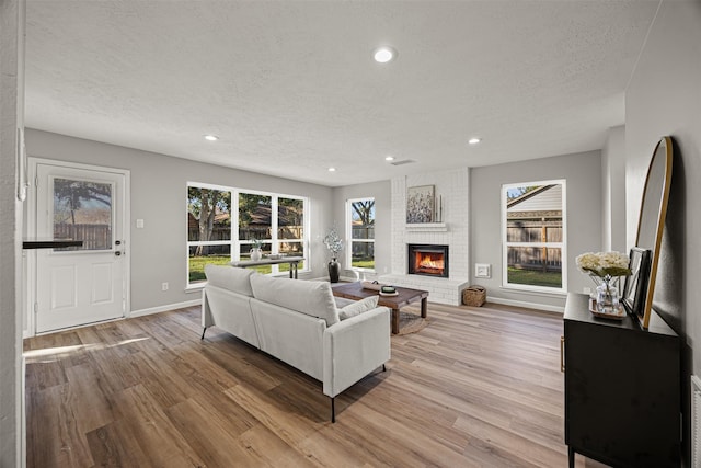 living room with light hardwood / wood-style floors, a textured ceiling, and a brick fireplace