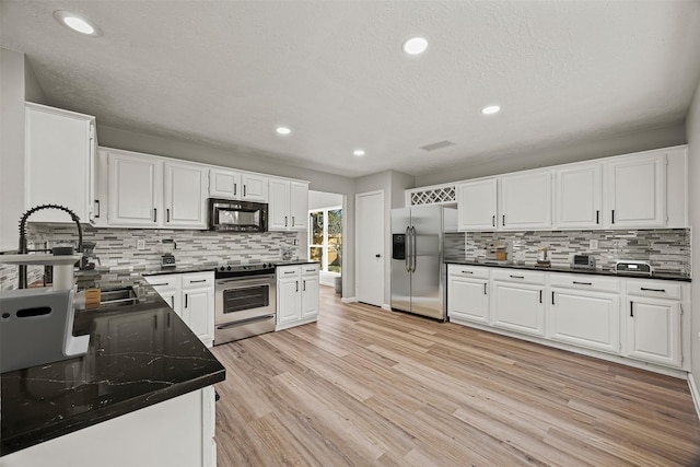 kitchen featuring white cabinetry, stainless steel appliances, backsplash, dark stone counters, and light wood-type flooring