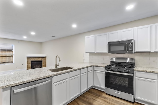 kitchen with stainless steel appliances, sink, hardwood / wood-style flooring, white cabinetry, and a tiled fireplace