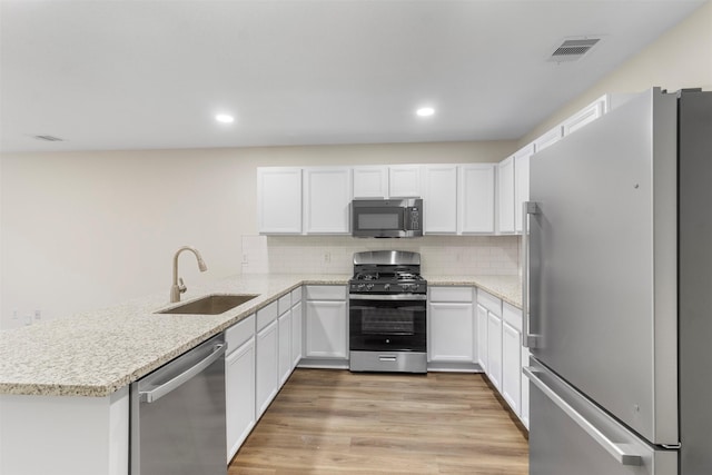 kitchen featuring white cabinetry, sink, kitchen peninsula, appliances with stainless steel finishes, and light wood-type flooring