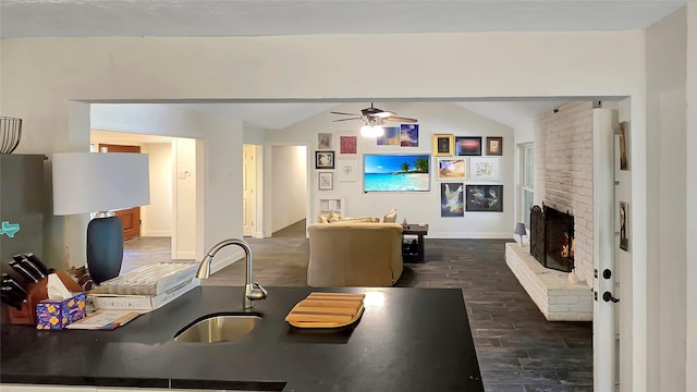 kitchen featuring ceiling fan, sink, dark wood-type flooring, a brick fireplace, and vaulted ceiling