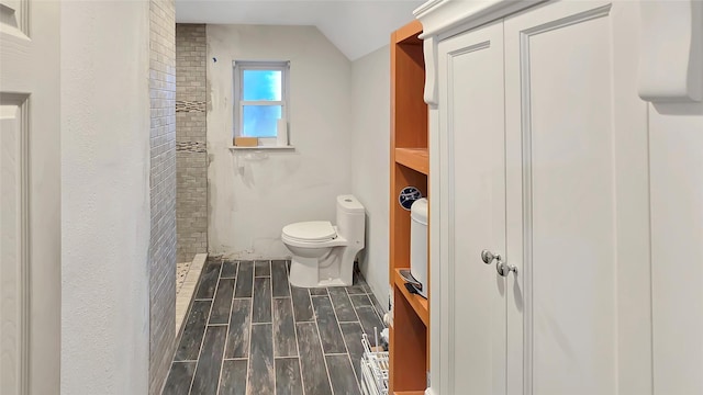 bathroom with toilet, lofted ceiling, and a tile shower