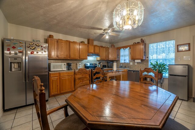 tiled dining space featuring ceiling fan with notable chandelier and a textured ceiling