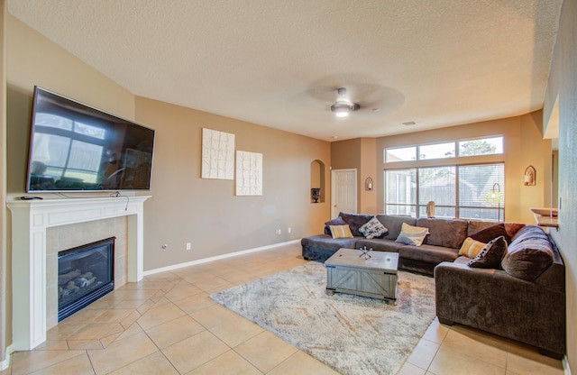 living room with ceiling fan, light tile patterned floors, a textured ceiling, and a tile fireplace