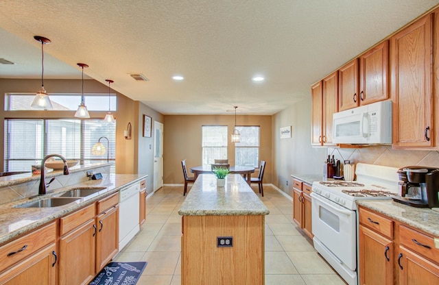 kitchen with sink, hanging light fixtures, light stone counters, white appliances, and a kitchen island