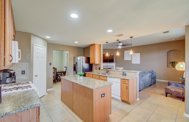 kitchen featuring white appliances, sink, hanging light fixtures, light stone countertops, and a kitchen island