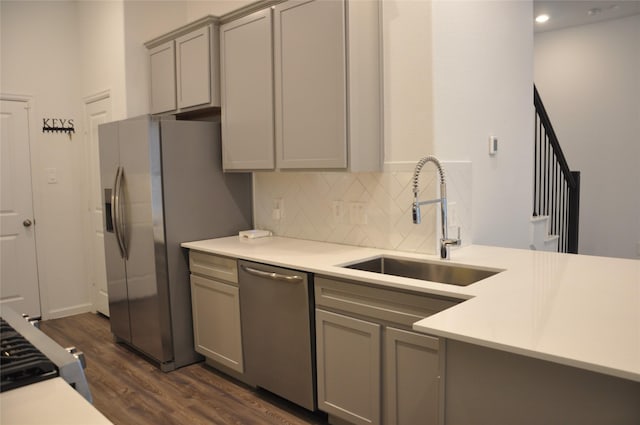 kitchen with gray cabinetry, sink, dark wood-type flooring, stainless steel appliances, and backsplash