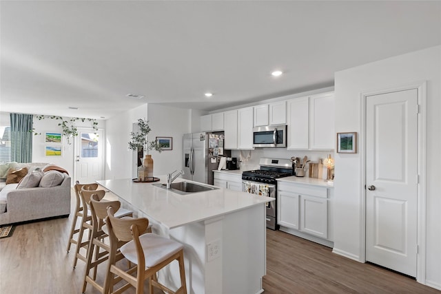 kitchen with white cabinets, a kitchen bar, stainless steel appliances, and a kitchen island with sink