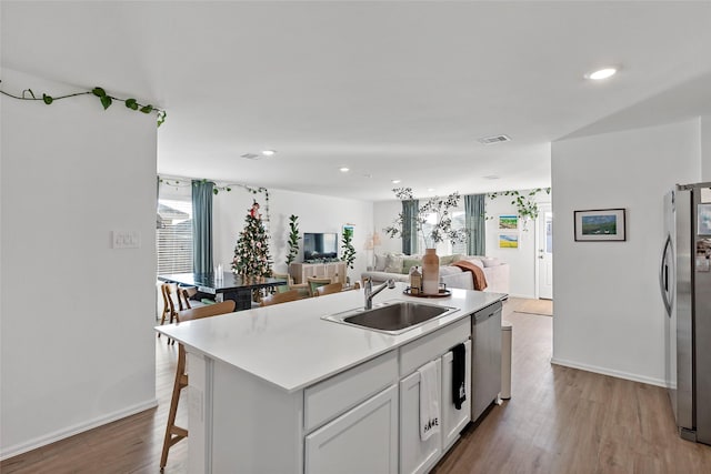 kitchen with a kitchen island with sink, a kitchen breakfast bar, sink, white cabinetry, and stainless steel appliances