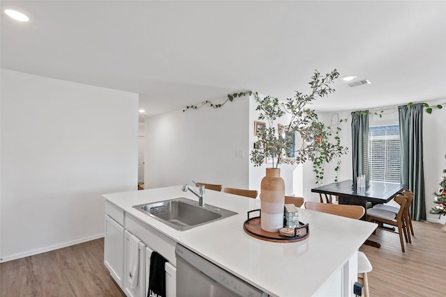 kitchen featuring stainless steel dishwasher, a kitchen island with sink, sink, white cabinets, and light hardwood / wood-style floors