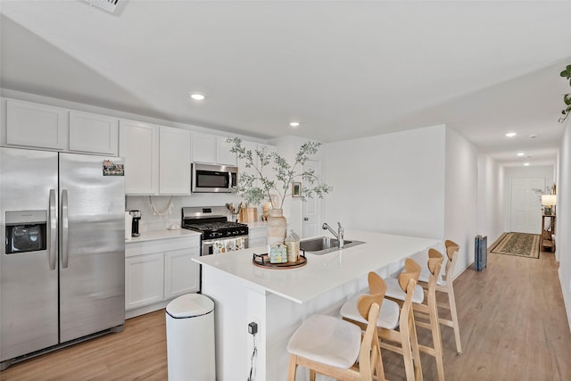 kitchen with white cabinets, a kitchen breakfast bar, sink, appliances with stainless steel finishes, and light hardwood / wood-style floors