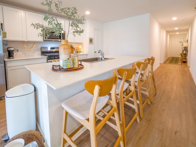 kitchen with a breakfast bar, light wood-type flooring, stainless steel appliances, white cabinetry, and a sink