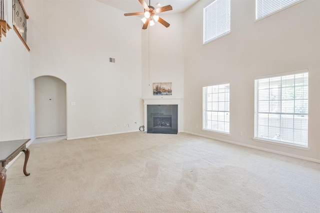 unfurnished living room with a tiled fireplace, light carpet, and ceiling fan