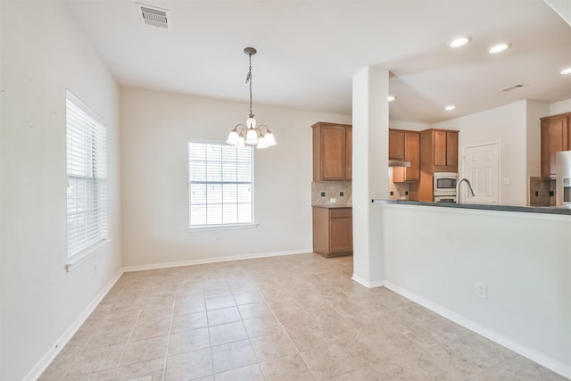 kitchen with pendant lighting, stainless steel microwave, a healthy amount of sunlight, and backsplash